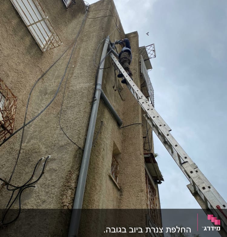 אדם על סולם מתקן צינור חיצוני על קיר בניין